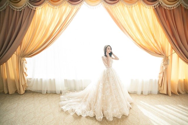 Dívka-nevěsta stojící u okna ve velkém sále